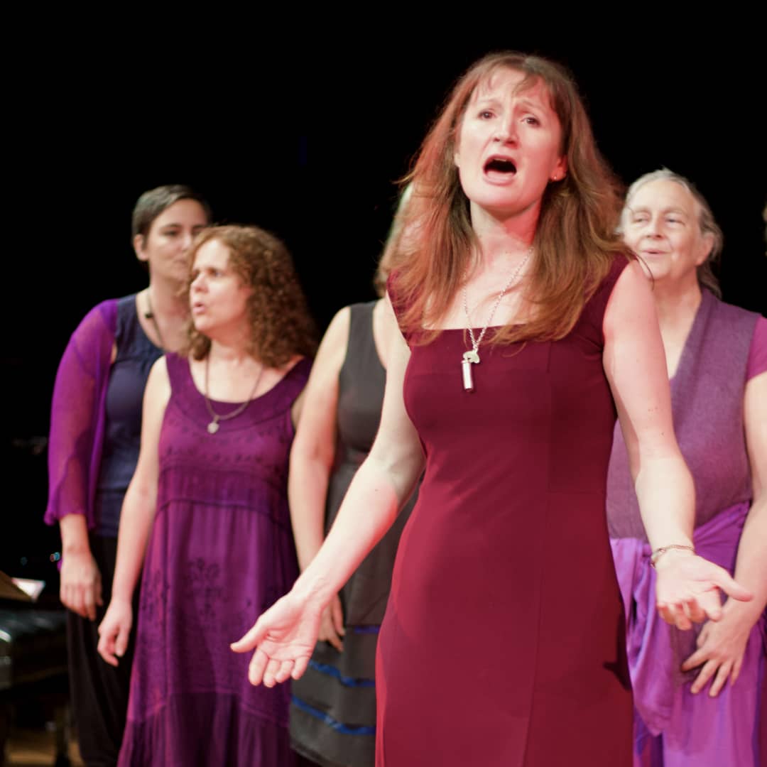 WolfSong choir performing at Byron Bay Theatre, singers holding open vowel ‘aaah’ with Imogen Wolf performing