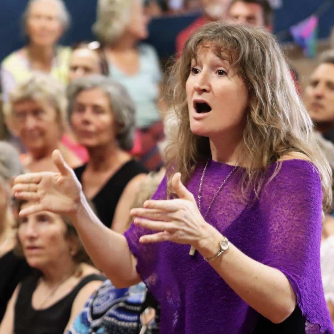 Imogen Wolf conducting SeaSong choir during a performance with audience in background
