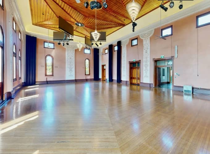 Spacious main hall at Glebe Town Hall with polished timber floors, high decorative walls and timber ceiling.
