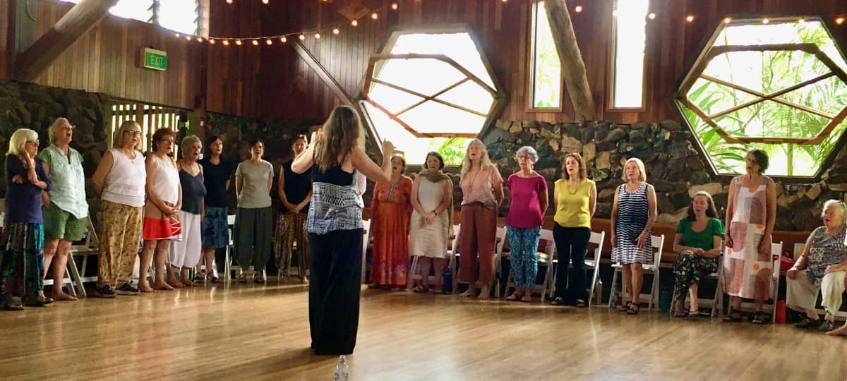 Wide shot of singers standing in a large circle inside Hanging Rock Hall with Imogen Wolf conducting
