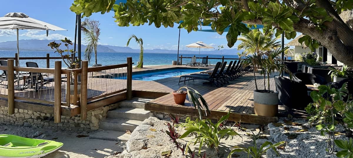 Beachfront swimming pool overlooking the ocean, with shaded deck seating, tropical gardens and distant island views.