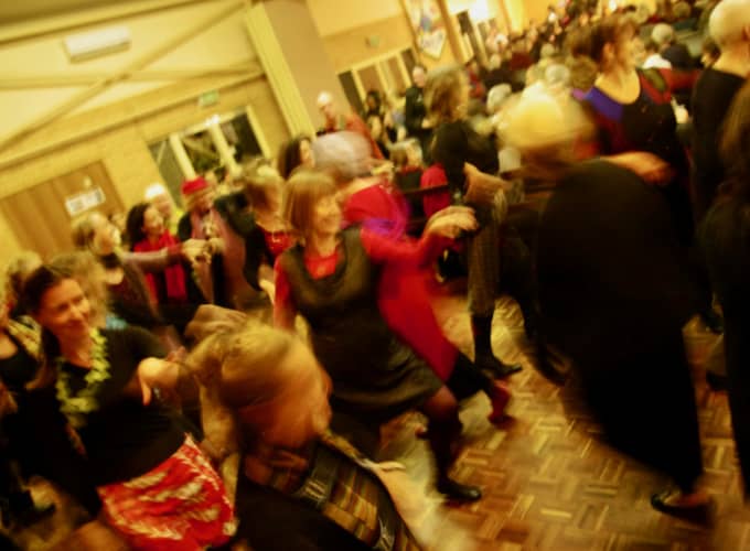 Participants dancing energetically together in a crowded hall during a WolfSong winter camp event.